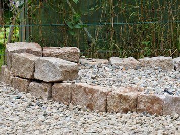 Kleine Natursteinmauer und Naturstein Schotter im Außenanlagen-Bereich
